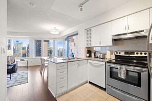 A modern kitchen with a large island, stainless steel appliances, and a view of the city through large windows. - Free Parking! Huge 3BR CityPlace Condo | Parking Available (Toronto)