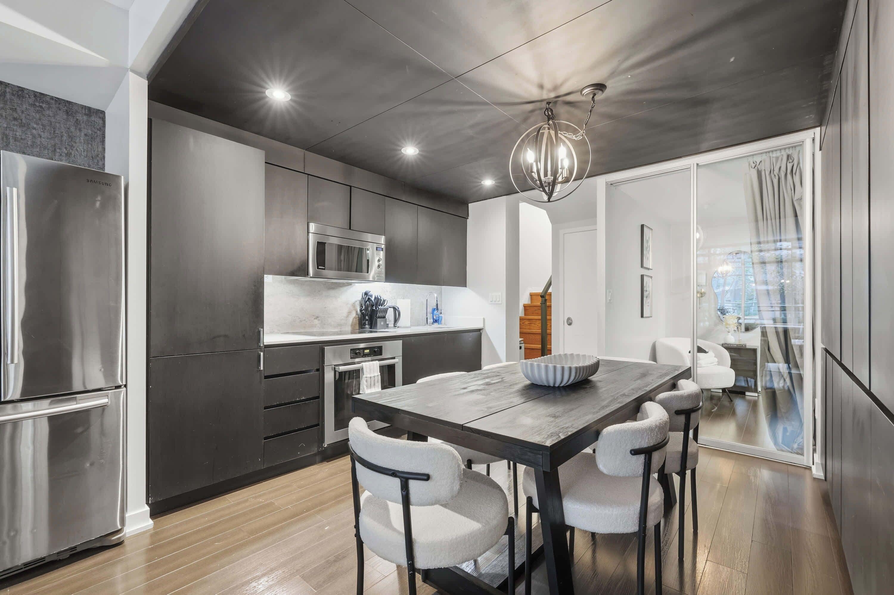 Una cucina moderna con elettrodomestici in acciaio inossidabile, un tavolo da pranzo con sedie e una lampada a sospensione.