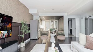 A modern living room with a flat-screen TV, a potted plant, a sofa, and a coffee table. - Luxury DT Townhome Steps to Top Attractions! (Toronto)
