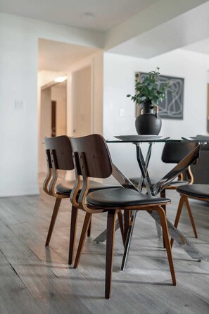 A modern dining area with a glass table, wooden chairs, and a potted plant. - Luxury Waterfront Escape Stylish 3BR Condo | Parking Available (Toronto)