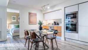 Een moderne keuken met een glazen eettafel, houten stoelen en roestvrijstalen apparatuur.
