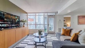 Een moderne woonkamer met een flatscreen televisie, een bank, een salontafel en een groot raam met uitzicht op de stad.