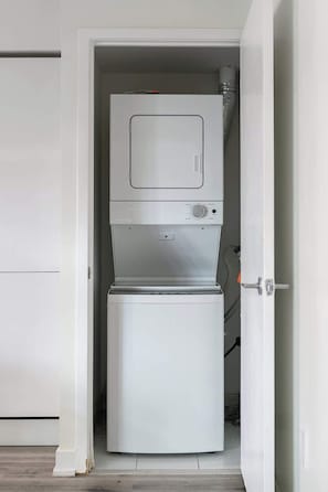 A compact, white, two-door appliance with a control panel and a small window on the upper door, likely a washer and dryer unit. - Luxury Waterfront Escape Stylish 3BR Condo | Parking Available (Toronto)