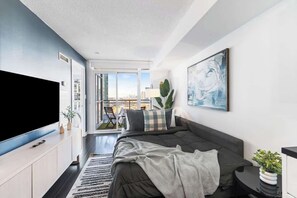 A modern living room with a large flat-screen TV, a sofa, and a dining area with chairs. - Downtown Central - Rogers Centre - 3 beds - Views (Toronto)