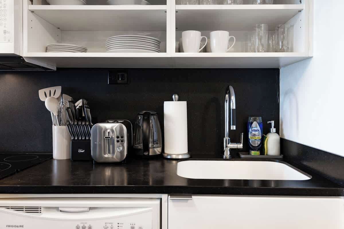 A kitchen with a black countertop, white cabinets, a dishwasher, and various kitchen utensils and appliances.
