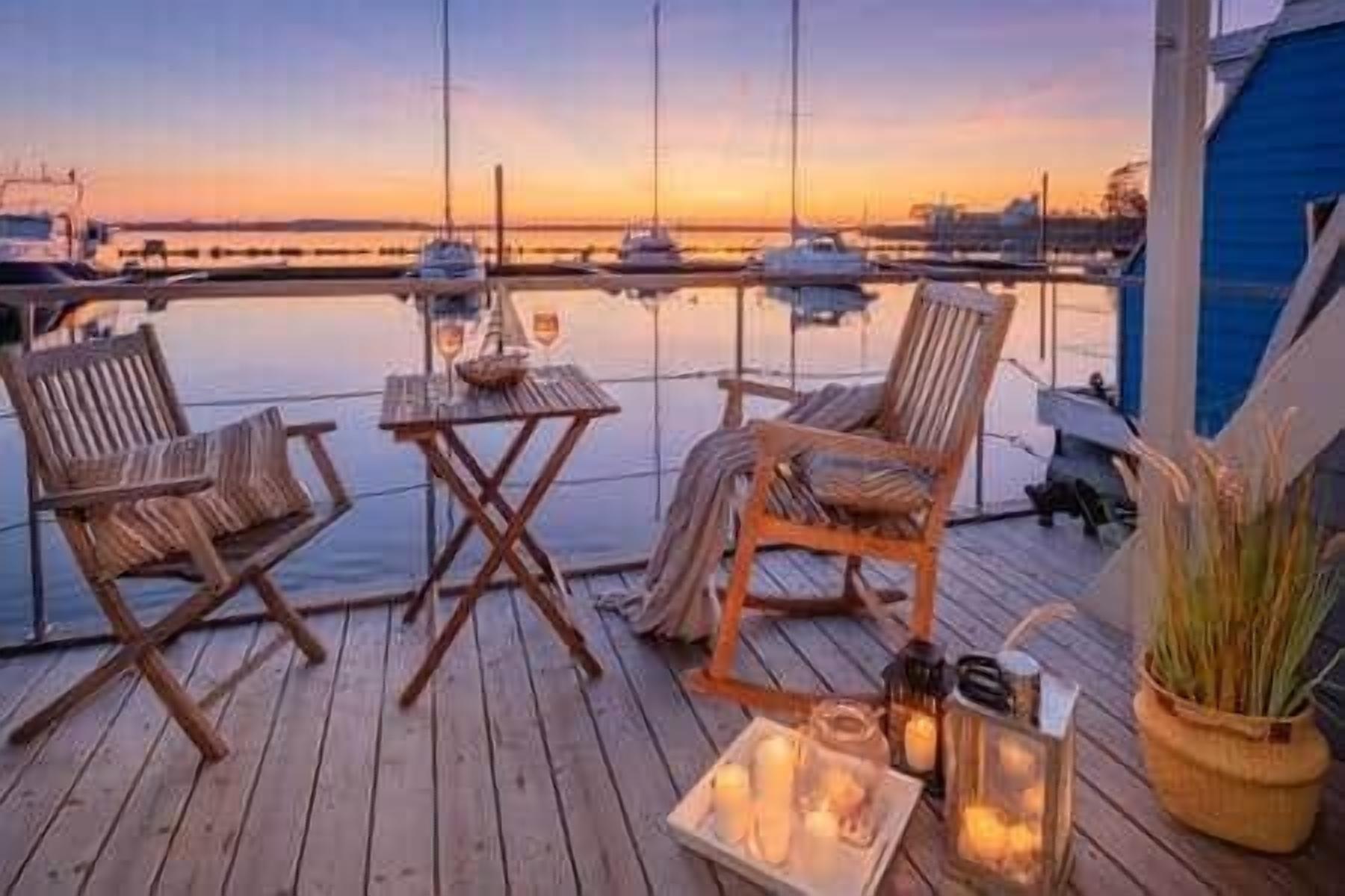 A wooden deck with two chairs and a table, overlooking a marina with boats.
