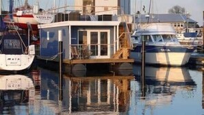 A dock with boats, a floating structure, and a building in the background. - Bosse Houseboat - Fehmarn, Burgstaaken (Fehmarn)