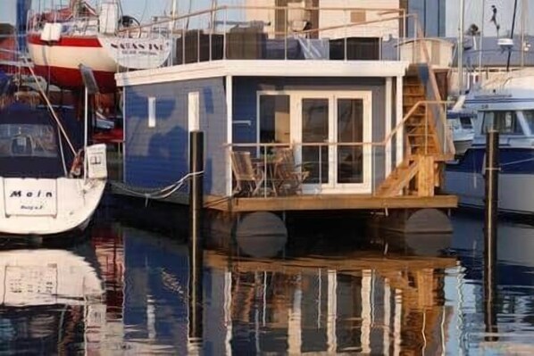 A docked houseboat with a staircase leading to the upper deck, surrounded by other boats.