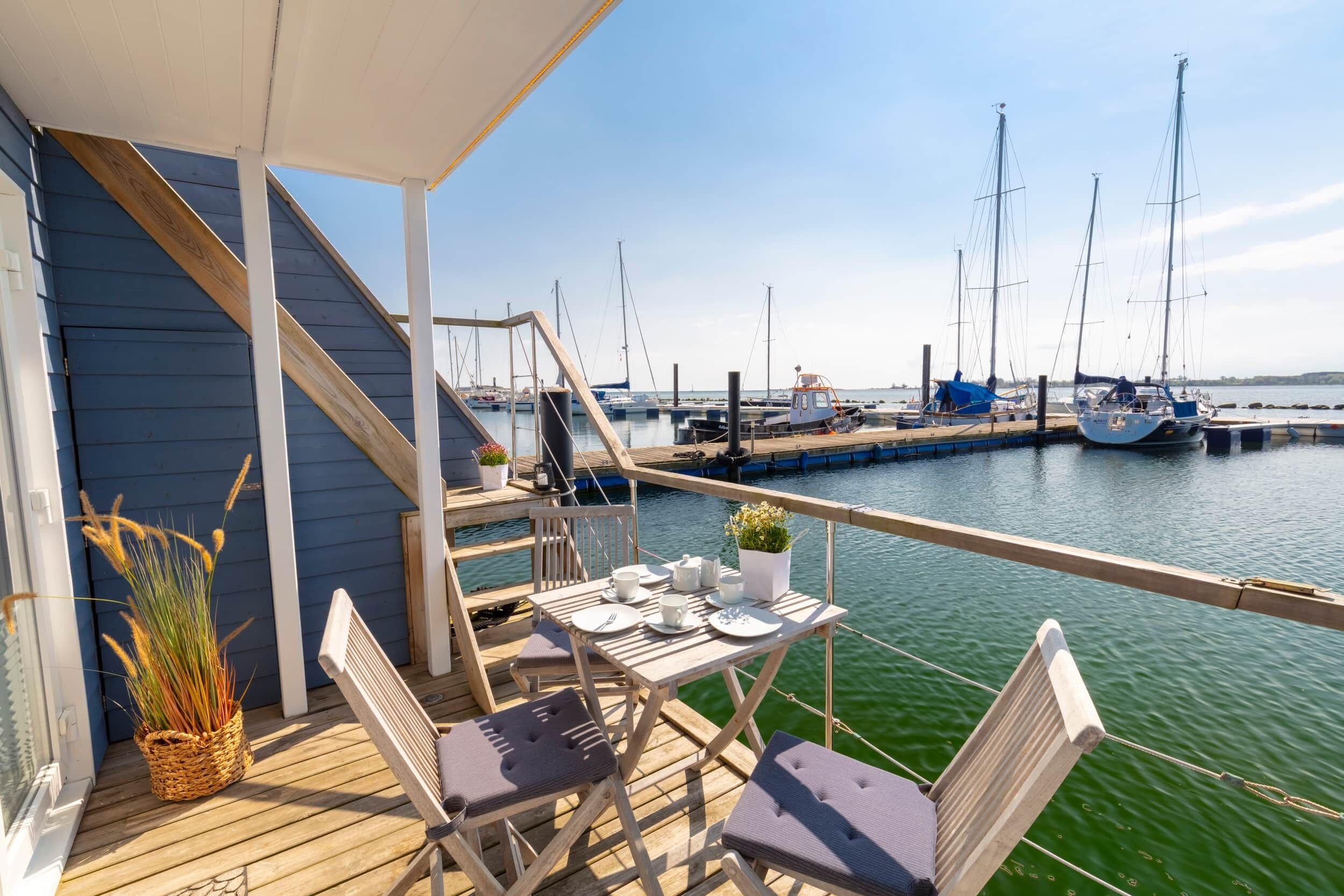 A wooden deck with a table set for two, overlooking a marina with sailboats.