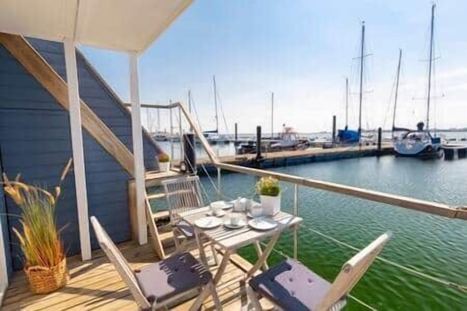 Un espacio de estar al aire libre cubierto con una mesa preparada para dos, con vistas a un puerto deportivo y barcos.