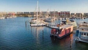 En småbåtshamn med flera förtöjda båtar, en strandpromenad och byggnader i bakgrunden.