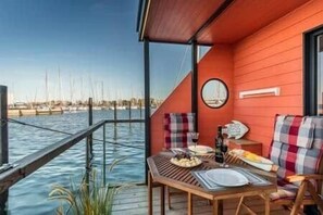 A red room with a table set for two, a clock on the wall, and a view of the water. - Isa-Bella Houseboat - Fehmarn, Burgtiefe (Fehmarn)