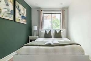 A bedroom with a bed, a nightstand, a lamp, and two abstract paintings on the wall.