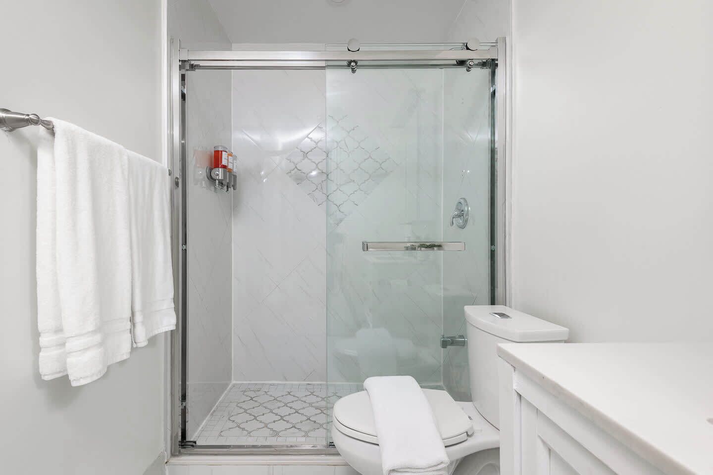 A modern bathroom with a glass-enclosed shower, a toilet, and a white towel on the wall.