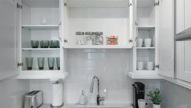 A kitchen with white cabinetry, a stainless steel sink, a toaster, a kettle, and a potted plant.
