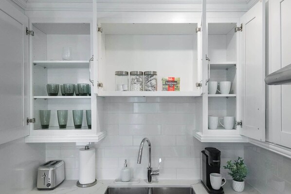A kitchen with white cabinetry, a stainless steel sink, a toaster, a kettle, and a potted plant.