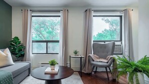 A living room with a sofa, armchair, round coffee table, and potted plants.