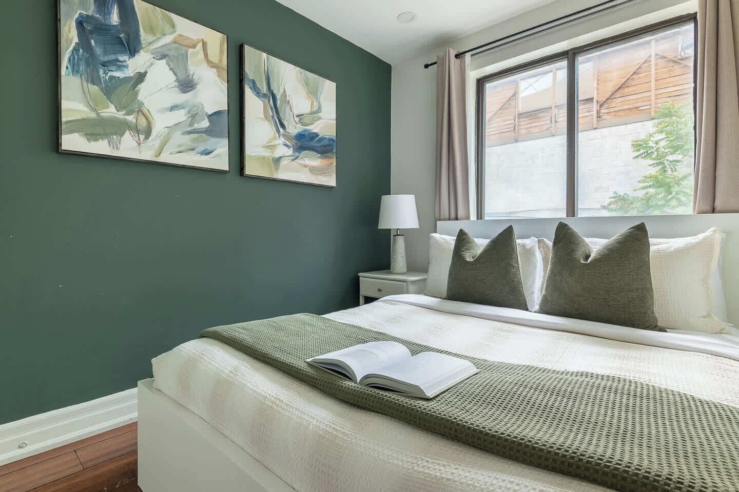 A bedroom with a bed, a nightstand, a lamp, and two abstract paintings on the wall.