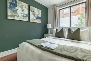 Un dormitorio con cama, mesita de noche, lámpara y dos cuadros abstractos en la pared.