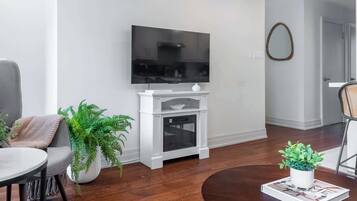 A modern living room with a flat-screen TV mounted on a white entertainment unit, a grey sofa, a round coffee table, and a potted plant.