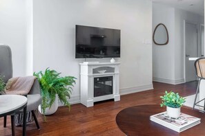 Una sala de estar moderna con un televisor de pantalla plana montado en un mueble blanco, un sofá gris, una mesa de centro redonda y una planta en maceta.