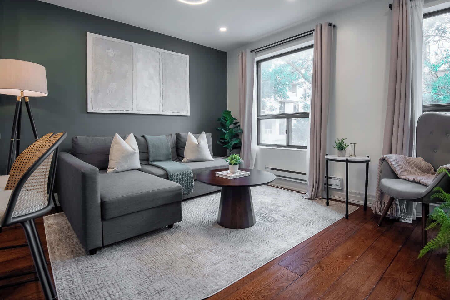 A modern living room with a sectional sofa, a round coffee table, and a large window with curtains.