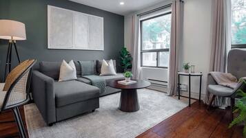 A modern living room with a sectional sofa, a round coffee table, and a large window with curtains.