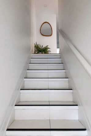 Una escalera con peldaños blancos y bordes negros, que conduce a un rellano con un espejo de marco de madera y una planta en maceta.