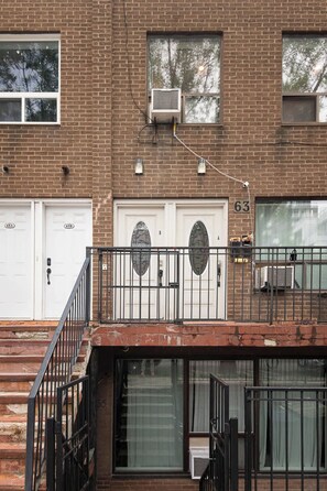 A two-story brick building with numbered garage doors, a metal staircase, and a small balcony with a railing.