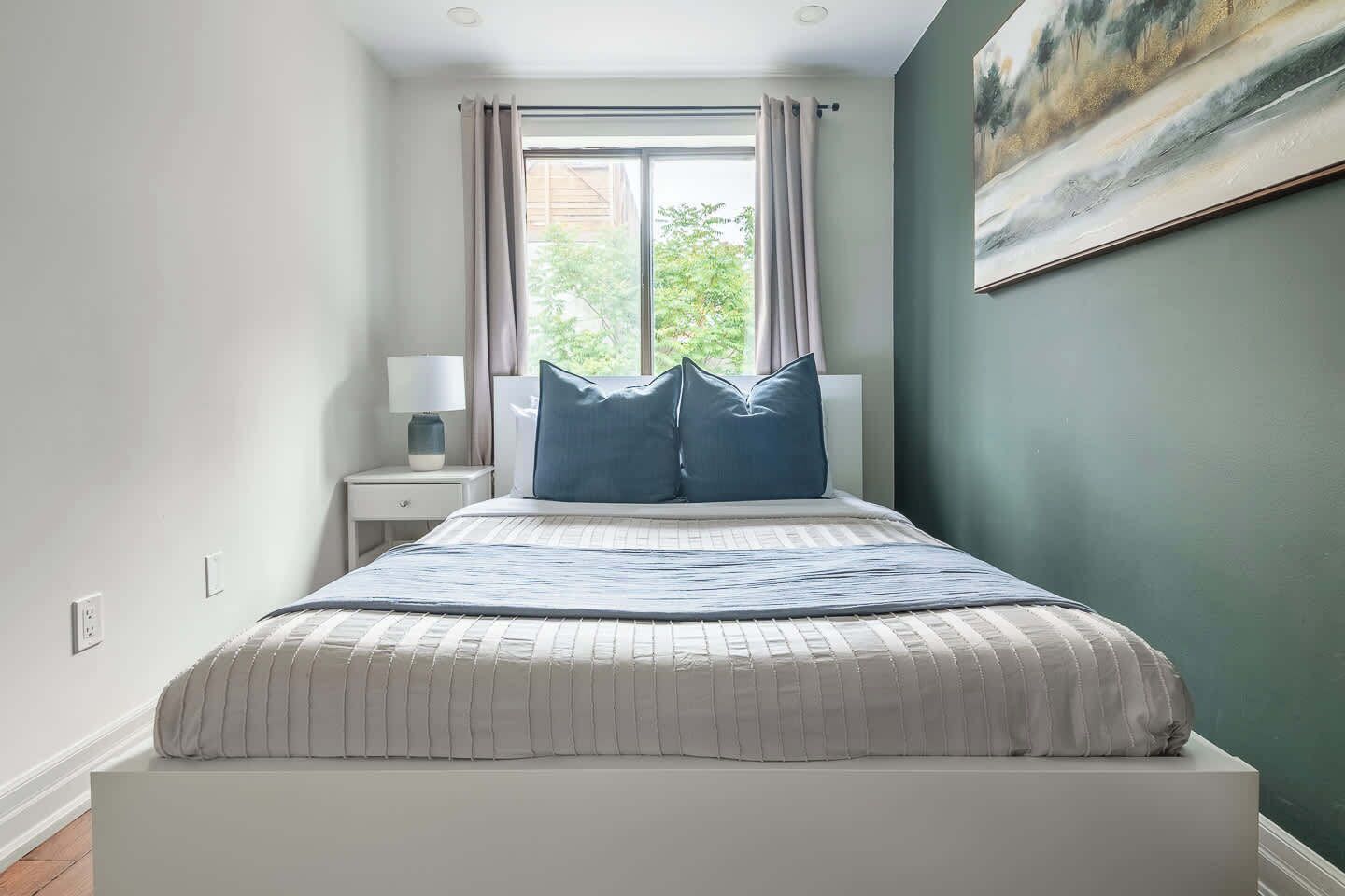 A bedroom with a bed, a nightstand, a lamp, and a painting on the wall.