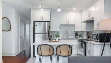 A modern kitchen with white cabinets, stainless steel appliances, and a central island with two bar stools.