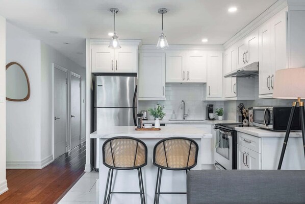 A modern kitchen with white cabinets, stainless steel appliances, and a central island with two bar stools.
