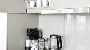 Eine moderne Küche mit eingebauten Schränken, einer Edelstahl-Dunstabzugshaube und einer Kaffeemaschine.