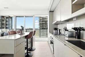 A modern kitchen with a large island, bar stools, and a view of the city through large windows. - Luxury 2BR Suite in Heart of Toronto Entertainment | Parking Available (Toronto)