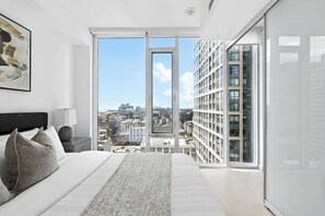 A modern bedroom with a large bed, a city view through a floor-to-ceiling window, and a cityscape visible outside. - Luxury 2BR Suite in Heart of Toronto Entertainment (Toronto)