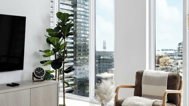 Ein modernes Wohnzimmer mit großem Fenster, Flachbildfernseher, Sofa, Couchtisch und einer Topfpflanze.