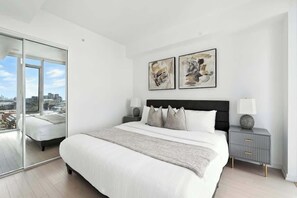 A modern bedroom with a large bed, a city view through a sliding door, and abstract art on the wall. - Luxury 2BR Suite in Heart of Toronto Entertainment | Parking Available (Toronto)