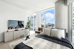 A modern bedroom with a large bed, a television, a city view, and a large window. - Luxury 2BR Suite in Heart of Toronto Entertainment | Parking Available (Toronto)