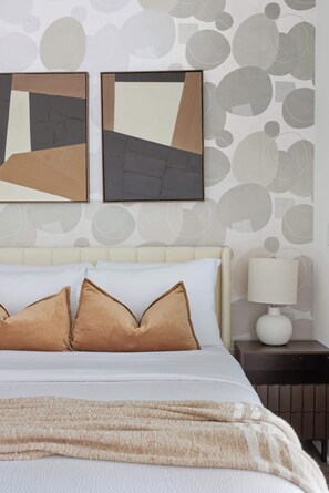 A hotel room with a bed, pillows, a nightstand, a lamp, and abstract wall art.