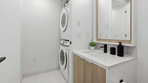 A modern bathroom with a built-in washing machine, a sink with a mirror above, and a small potted plant.