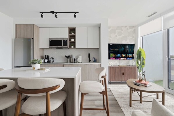 Une cuisine moderne dotée d’un îlot central, de tabourets de bar, d’un coin repas et d’un espace de vie avec un téléviseur.