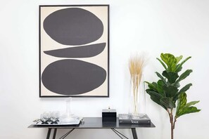 A framed abstract artwork, a vase with dried plants, and a potted plant on a table.
