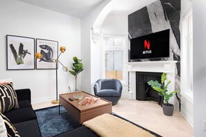 A modern living room with a fireplace, a sofa, a coffee table, and a TV mounted on a marble wall.