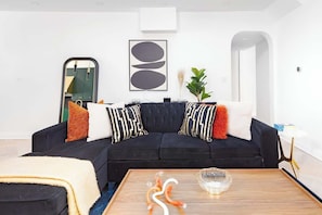 A modern living room with a black sectional sofa, a wooden coffee table, and a large mirror.