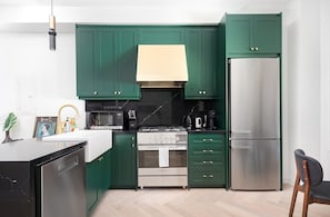 A modern kitchen with green cabinets, a stainless steel refrigerator, a stove, and a microwave.