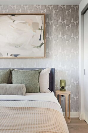 Une chambre à coucher avec un lit, des oreillers, une table de chevet et un mur orné d’un motif de feuilles.