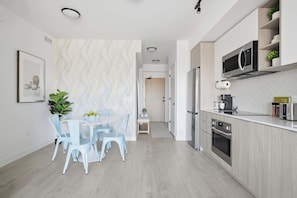 A modern kitchen with stainless steel appliances, a dining area with light blue chairs, and a patterned wall. - Bright Condo, Skyline Views & Balcony | Parking (Toronto)