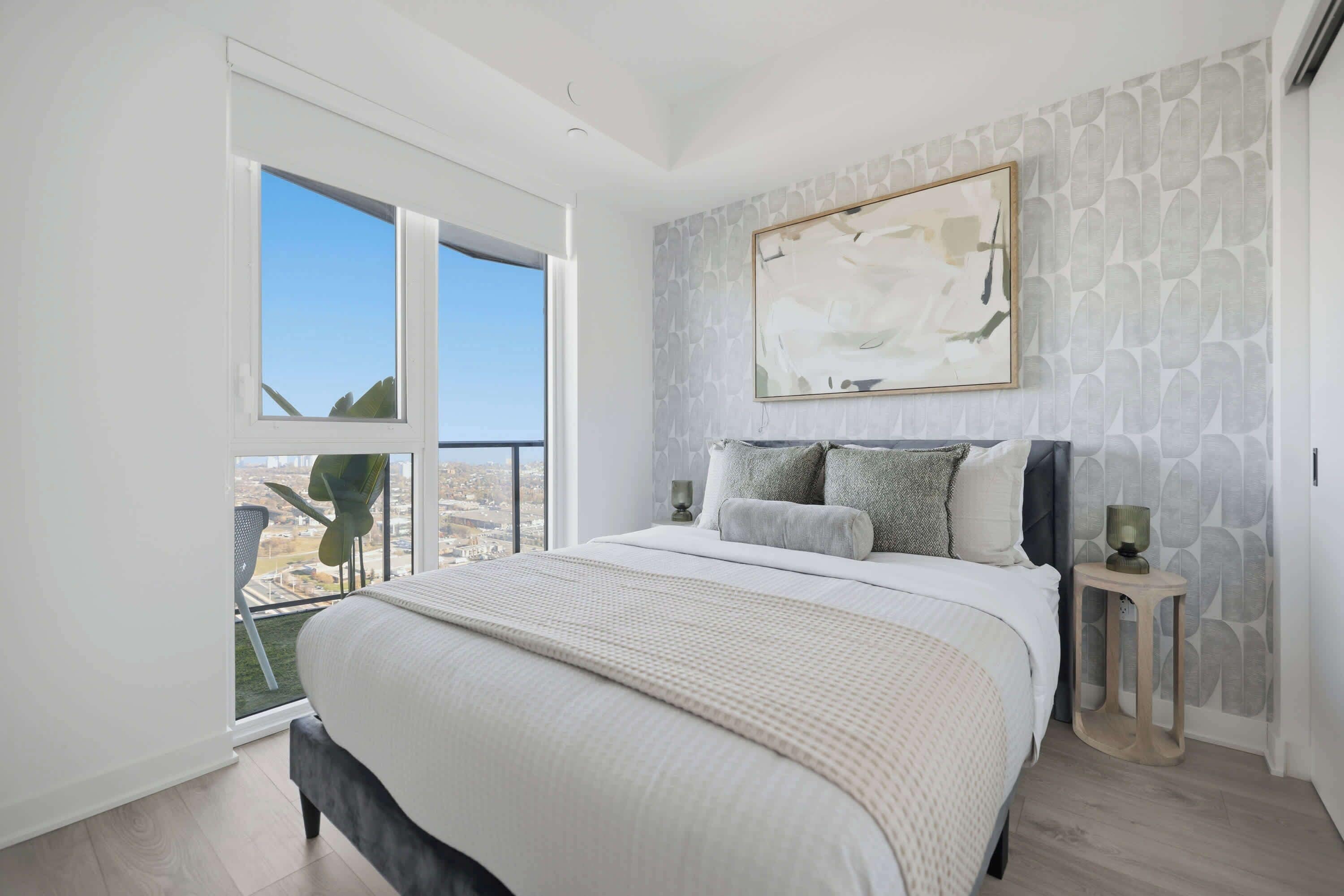 A bedroom with a large bed, a city view through a window, and a modern abstract painting on the wall.