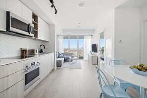 A modern kitchen with built-in appliances, a dining area with a table and chairs, and a view of the city through large windows. - Bright Condo, Skyline Views & Balcony | Parking (Toronto)