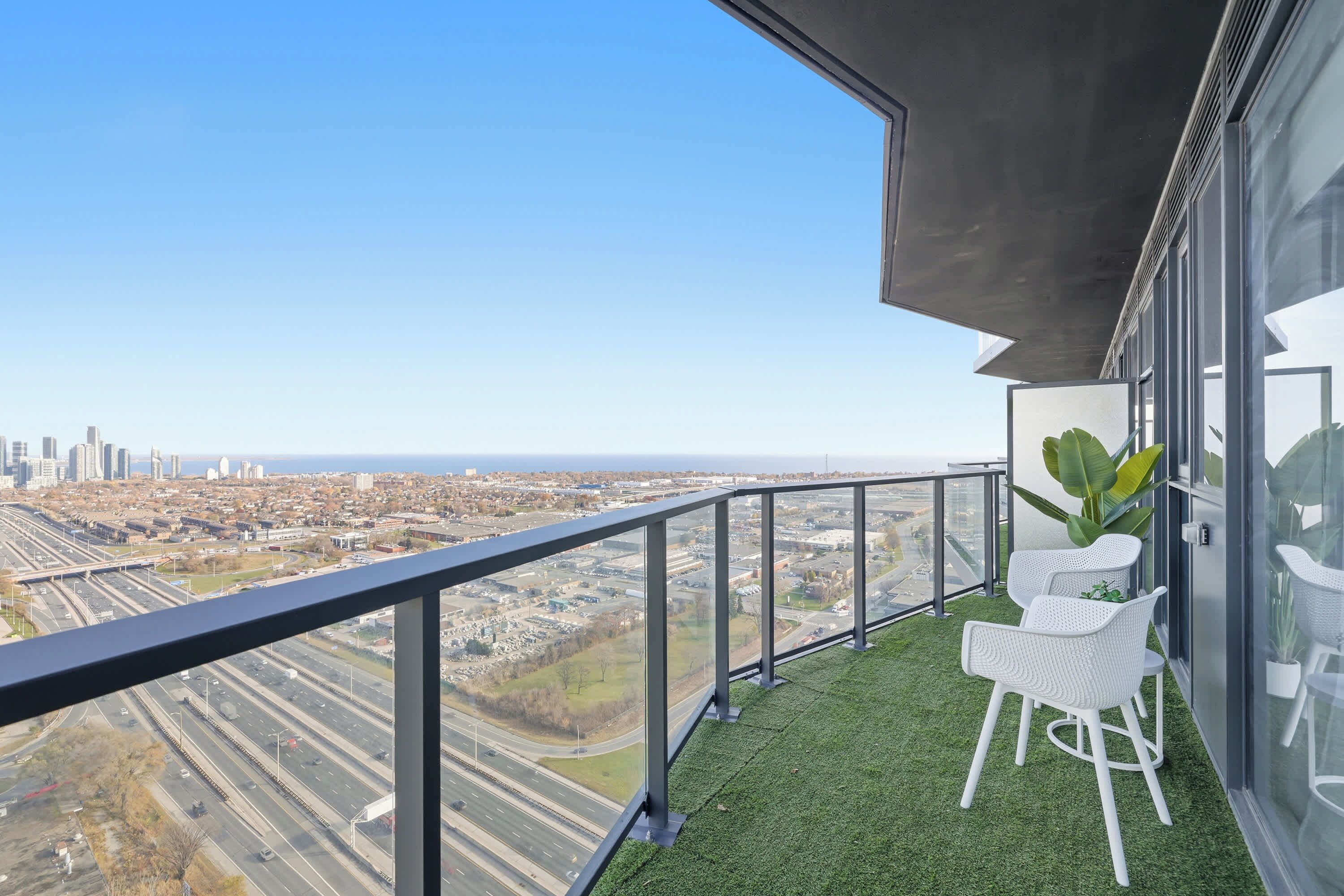 Een balkon met uitzicht over de stad, witte stoelen en een grote plant.